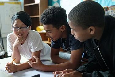 Three middle school students talk together in a classroom.